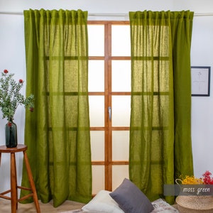 May include: Two moss green linen curtains hanging in front of a window with a wooden frame. The curtains are gathered at the top and have a relaxed, casual look.