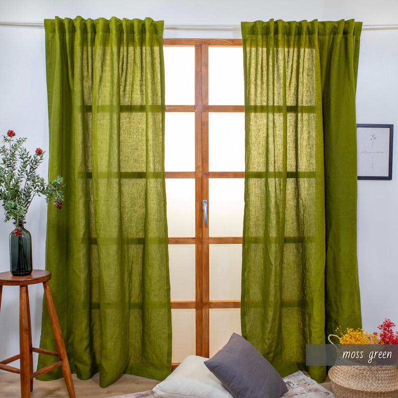 May include: Two moss green linen curtains hanging in front of a window with a wooden frame. The curtains are gathered at the top and have a relaxed, casual look.