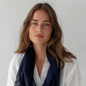 May include: A woman with long brown hair wearing a white button-down shirt and a dark blue scarf.