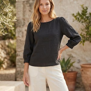 May include: A charcoal gray long-sleeved blouse with a round neckline and gathered puff sleeves featuring buttoned cuffs, paired with off-white wide-leg trousers that have a visible front button closure and side pockets.