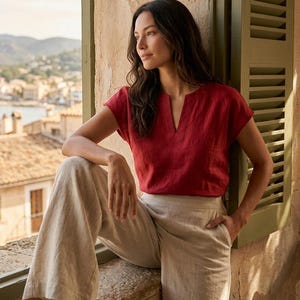 May include: A short-sleeved red blouse with a notched V-neckline paired with high-waisted beige wide-leg trousers. The blouse features a simple cut and the trousers include side pockets, creating a coordinated two-piece outfit ensemble.