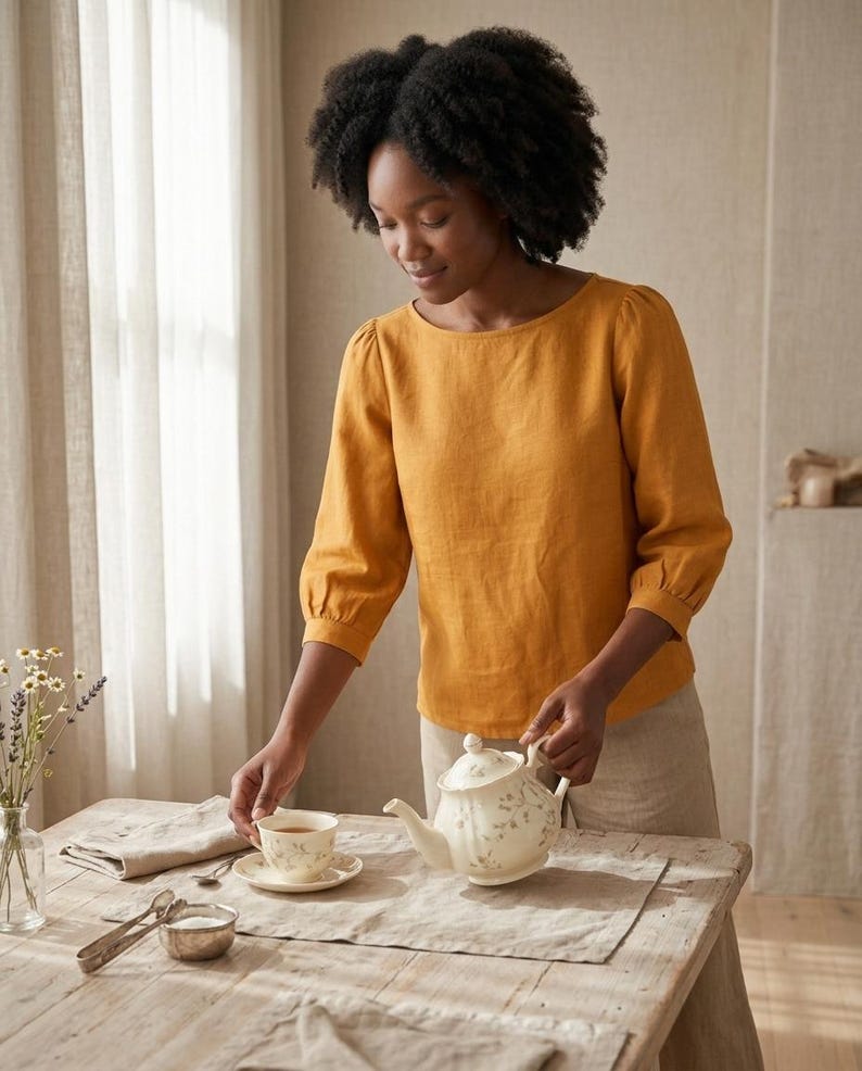 May include: A mustard yellow long-sleeved blouse with a round neckline and gathered sleeve cuffs, paired with light beige trousers. The blouse features a simple, solid-colored design with a relaxed fit and three-quarter length sleeves.