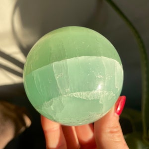May include: A green selenite sphere with white banding. The sphere is smooth and polished.