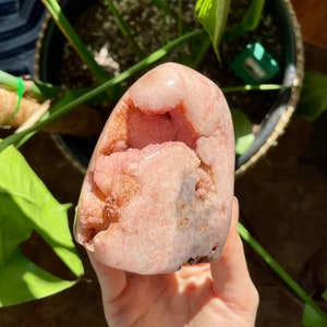 May include: A pink and white crystal with a natural, rough texture. The crystal has a large, open cavity in the center, revealing a pink and white interior.