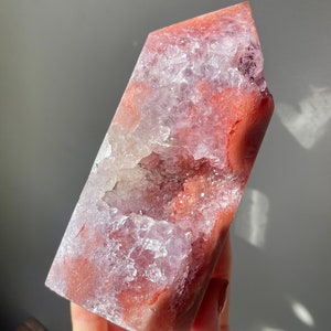 May include: A large, pink and red agate crystal with a natural, open geode. The crystal is polished and has a smooth, glassy surface.