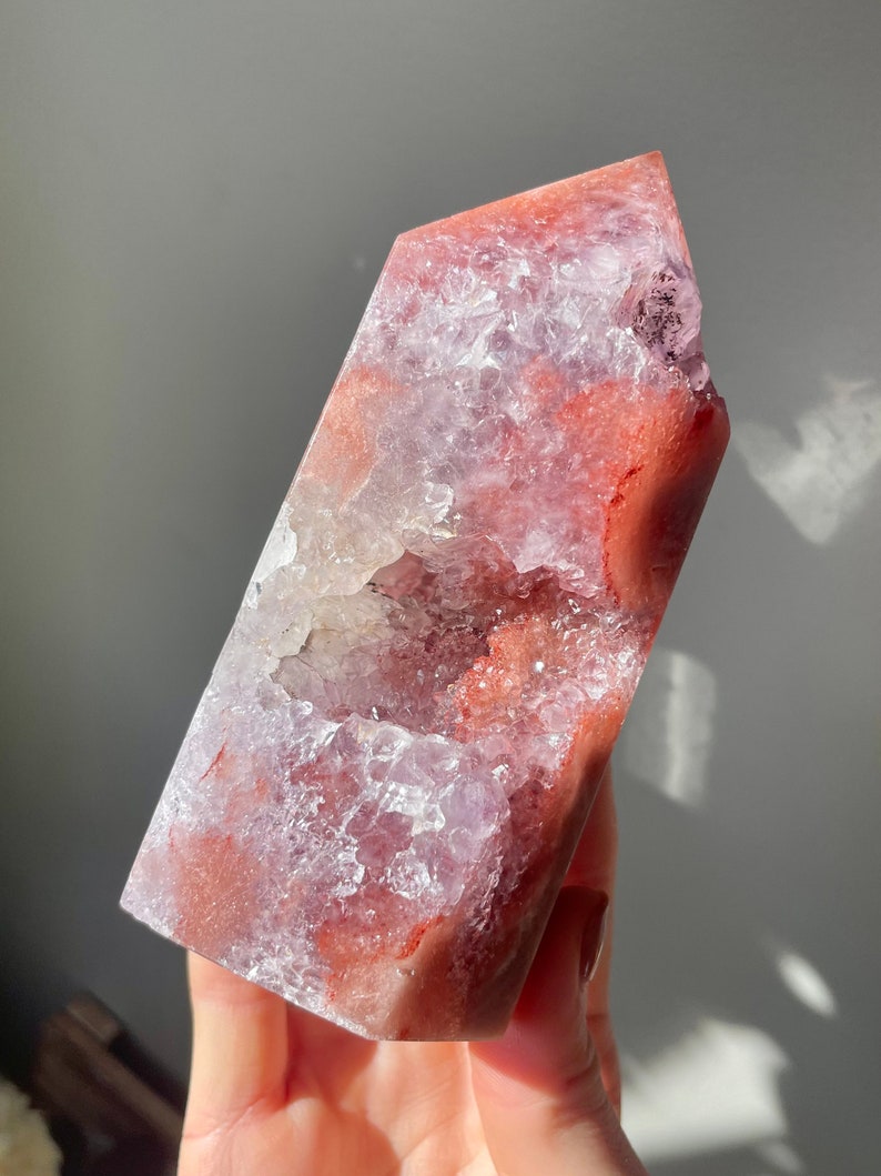May include: A large, pink and red agate crystal with a natural, open geode. The crystal is polished and has a smooth, glassy surface.