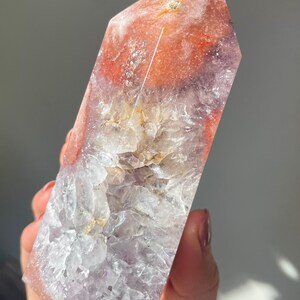 May include: A large, clear, amethyst crystal point with a pink and orange agate cap. The crystal is polished and has a smooth, glassy surface.