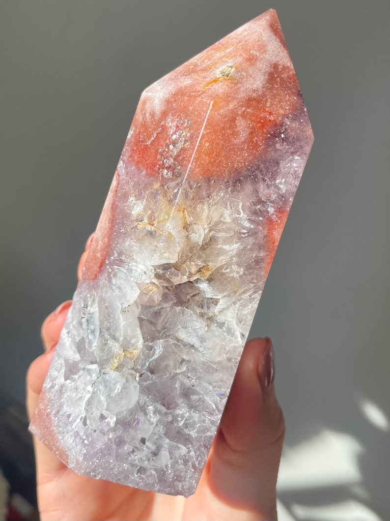 May include: A large, clear, amethyst crystal point with a pink and orange agate cap. The crystal is polished and has a smooth, glassy surface.
