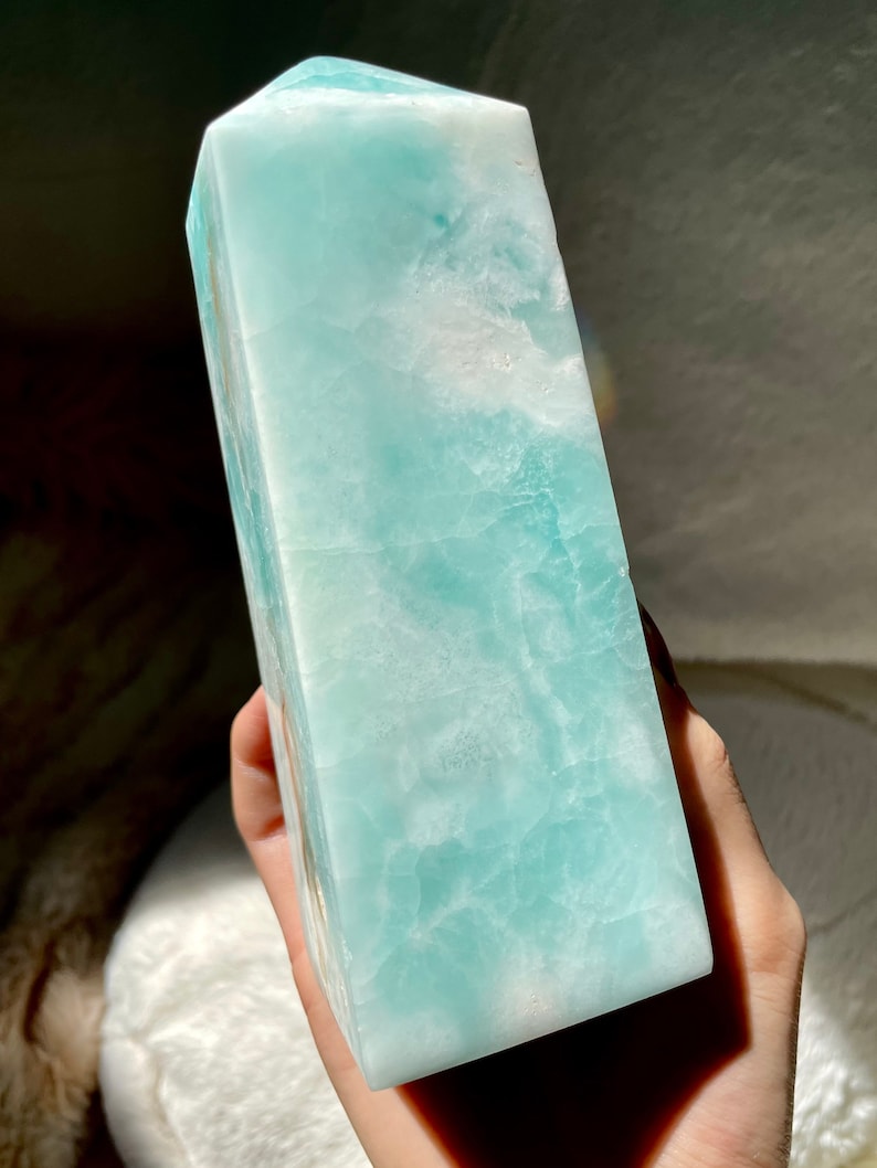 May include: A polished, tower-shaped crystal point featuring a smooth, translucent surface with a marbled pattern of light turquoise, pale blue, and opaque white mineral inclusions throughout the stone structure.