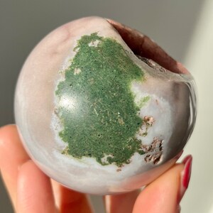 May include: A smooth, white and pink sphere with a large green patch. The sphere has a natural, polished finish.