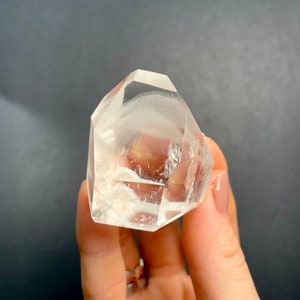 May include: A clear quartz crystal with a double terminated point, also known as a double-pointed crystal. The crystal is faceted and has a smooth, polished surface.