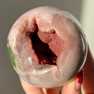 May include: A pink and white geode sphere with a large opening revealing a red and brown crystal interior.