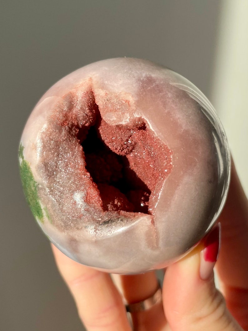 May include: A pink and white geode sphere with a large opening revealing a red and brown crystal interior.