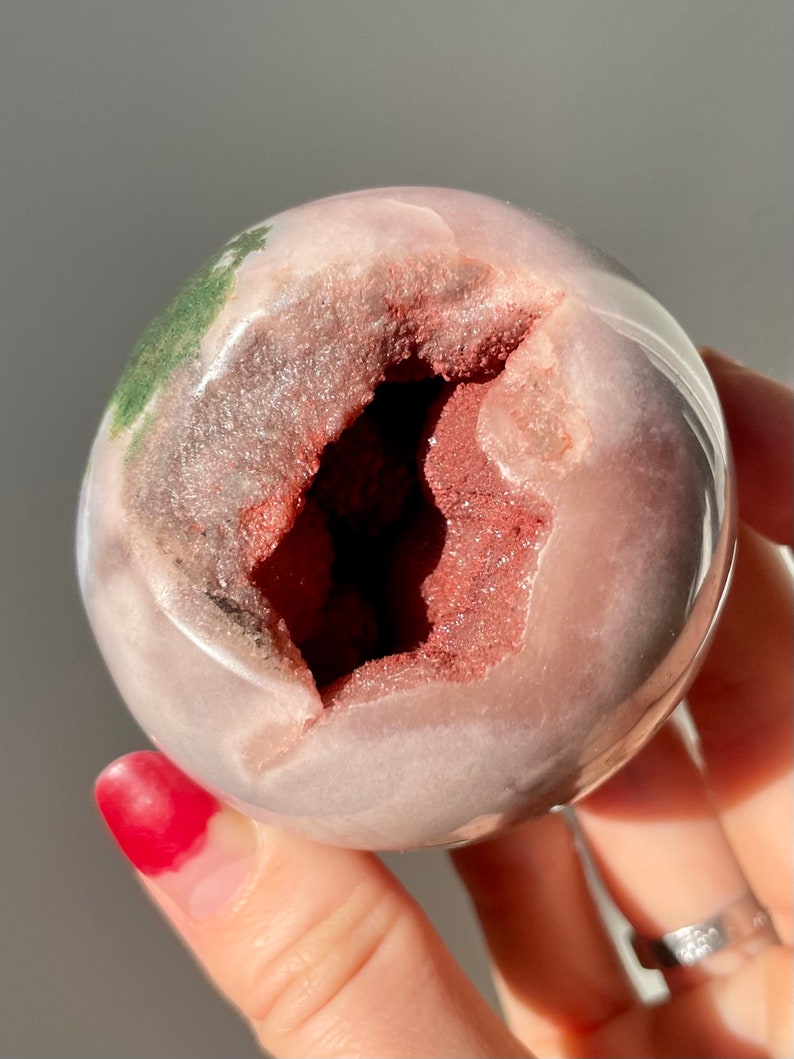 May include: A pink and white geode sphere with a large opening revealing a red and brown crystal interior. The sphere has a green and white pattern on the outside.