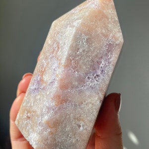 May include: A large, light purple and white crystal point with a rough, textured surface. The crystal has a pointed top and a flat base.