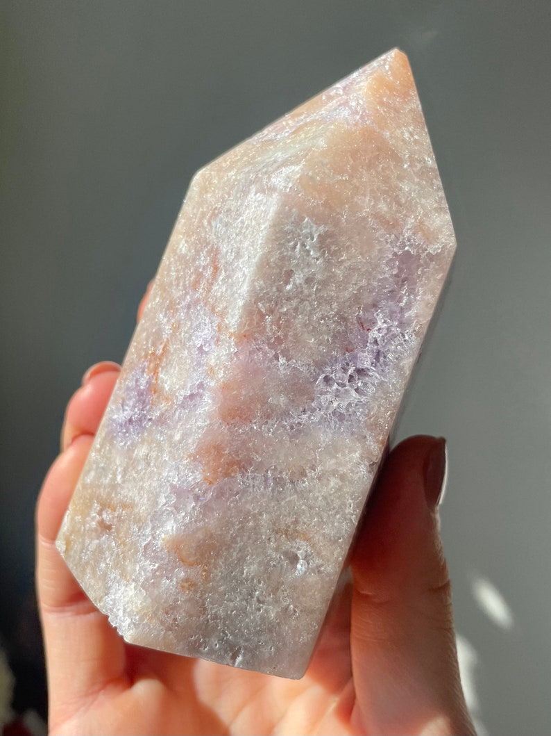 May include: A large, light purple and white crystal point with a rough, textured surface. The crystal has a pointed top and a flat base.