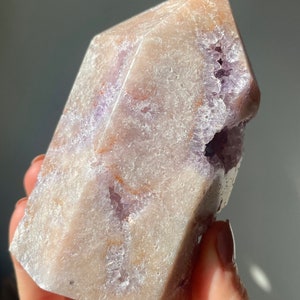 May include: A large, light purple amethyst crystal with a natural, rough texture. The crystal has a point at the top and a flat base. It has a natural, rough texture and is a beautiful example of a natural crystal.