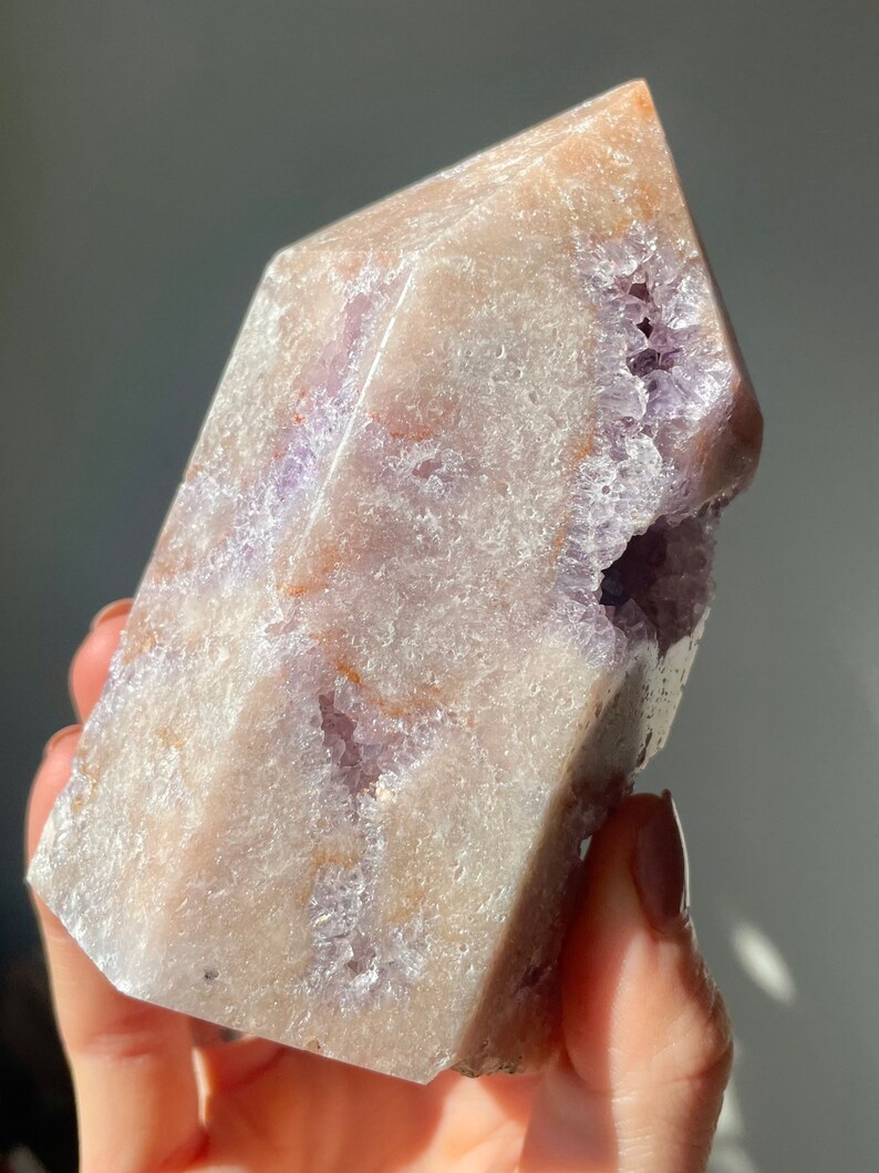 May include: A large, light purple amethyst crystal with a natural, rough texture. The crystal has a point at the top and a flat base. It has a natural, rough texture and is a beautiful example of a natural crystal.