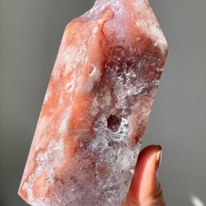 May include: A large, clear, pink and purple amethyst crystal point with a rough, natural texture. The crystal has a unique, layered appearance with a clear, glassy center and a pink and purple outer layer.