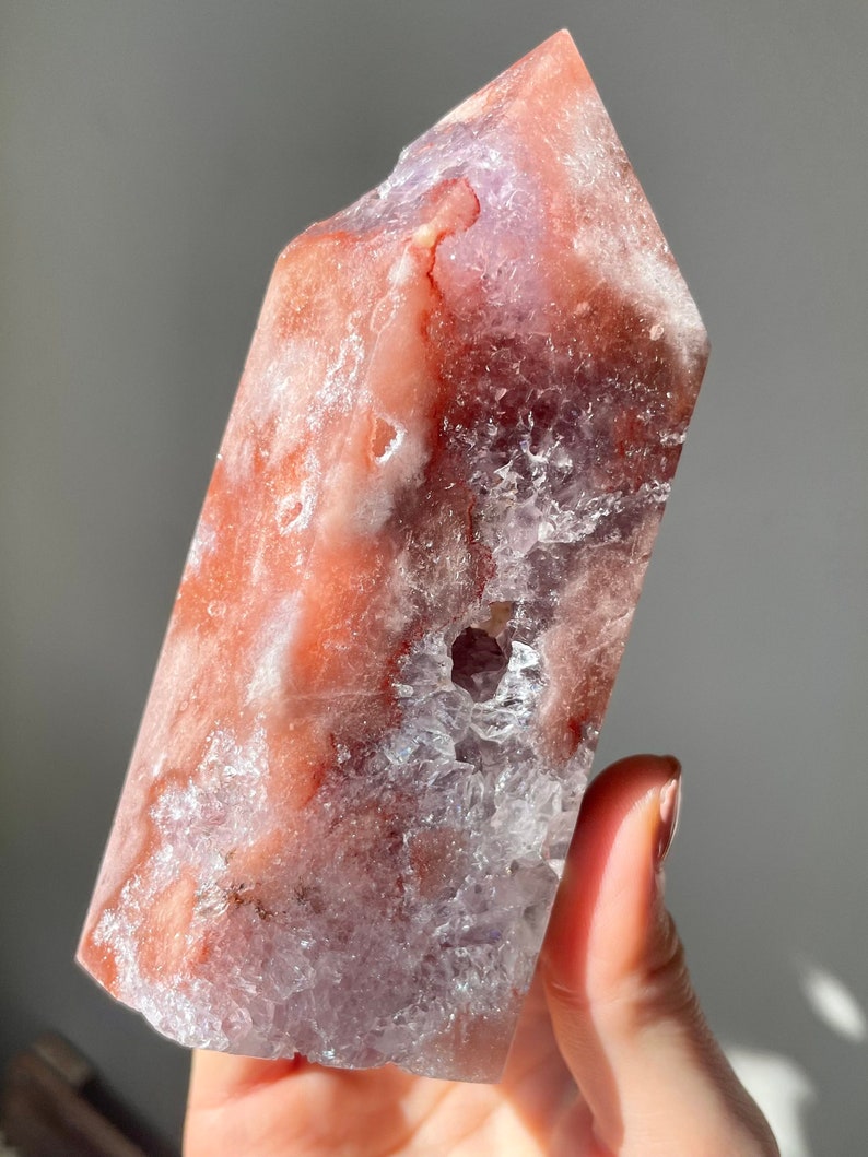 May include: A large, clear, pink and purple amethyst crystal point with a rough, natural texture. The crystal has a unique, layered appearance with a clear, glassy center and a pink and purple outer layer.