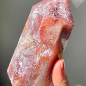 May include: A large, faceted, pink and white crystal with a clear, glassy texture. The crystal has a pointed top and a flat base.