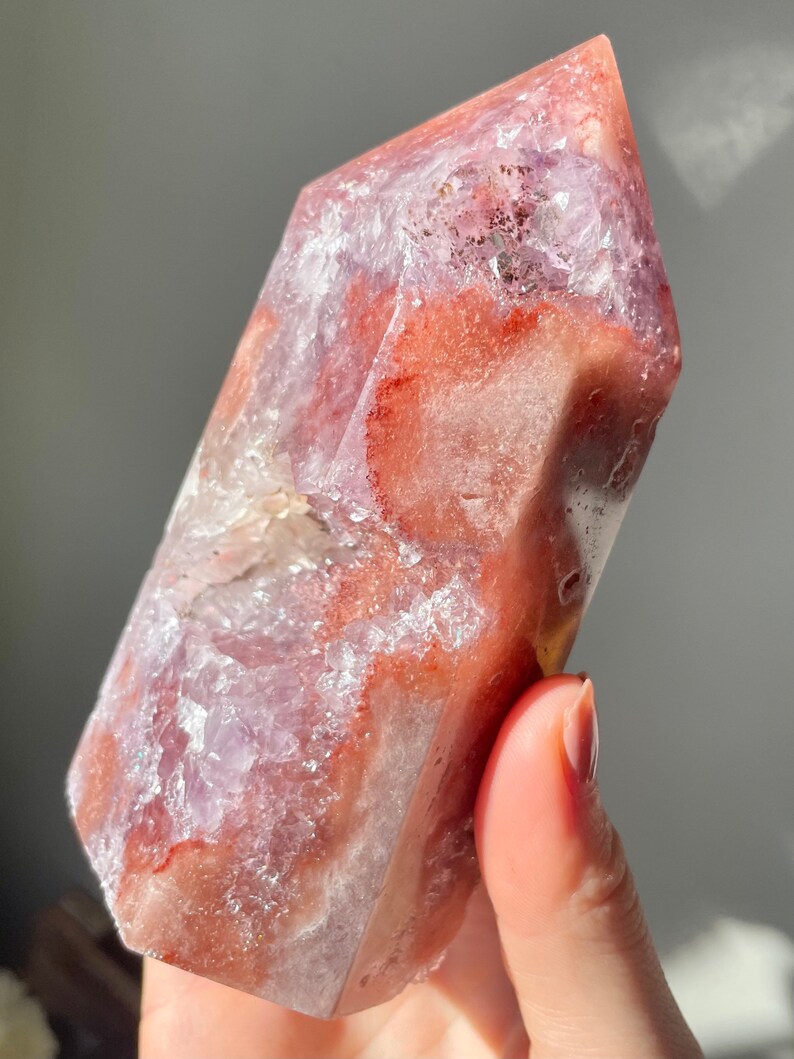 May include: A large, faceted, pink and white crystal with a clear, glassy texture. The crystal has a pointed top and a flat base.