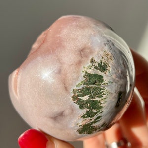 May include: A smooth, round, pink and white agate sphere with green moss inclusions. The sphere is about the size of a golf ball.