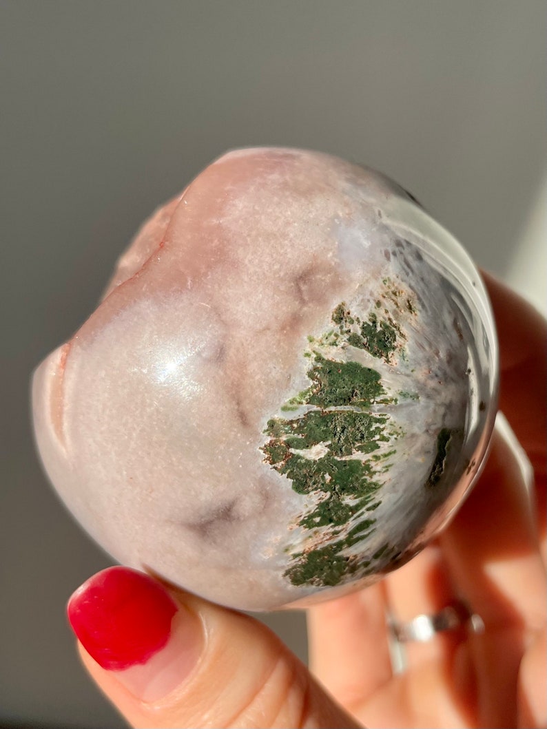 May include: A smooth, round, pink and white agate sphere with green moss inclusions. The sphere is about the size of a golf ball.