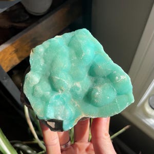 May include: A large, teal green, mineral specimen with a rough, textured surface. The mineral has a cluster of small, rounded formations.