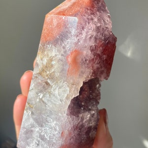 May include: A large, clear crystal point with a purple and red color gradient. The crystal has a natural, rough texture and a unique, asymmetrical shape.