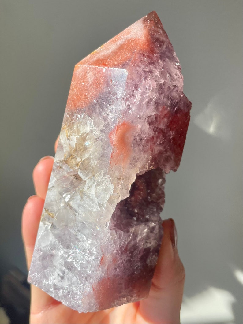 May include: A large, clear crystal point with a purple and red color gradient. The crystal has a natural, rough texture and a unique, asymmetrical shape.