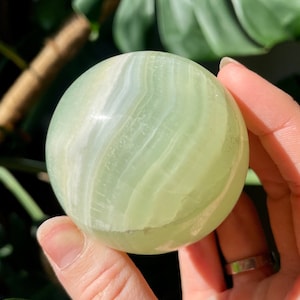 May include: A smooth, green and white, polished, sphere-shaped, green onyx crystal ball.
