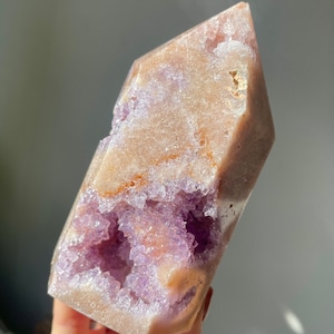 May include: A large, light pink amethyst crystal with a natural, raw, and rough texture. The crystal has a large, open cavity filled with smaller, purple amethyst crystals. The crystal is a natural, raw, and rough specimen.