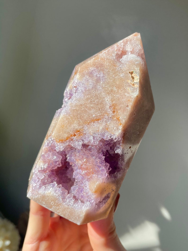 May include: A large, light pink amethyst crystal with a natural, raw, and rough texture. The crystal has a large, open cavity filled with smaller, purple amethyst crystals. The crystal is a natural, raw, and rough specimen.