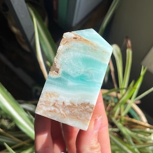 May include: A blue and brown celestite tower crystal. The crystal has a smooth, polished surface and is a light blue color with brown bands.