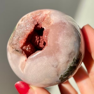May include: A pink and green geode sphere with a large opening revealing a red and pink crystal inside.