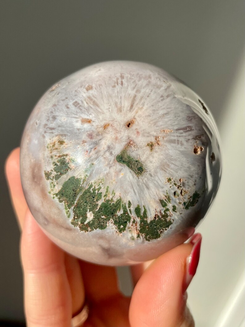May include: A white and green agate sphere with a unique, swirling pattern. The sphere is polished and smooth, with a natural, organic look.