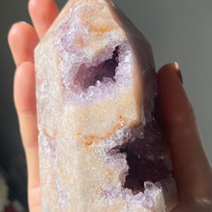 May include: A large, light purple amethyst crystal with a natural, hollowed-out center. The crystal has a pointed top and a flat base. The crystal is translucent and has a slight shimmer.