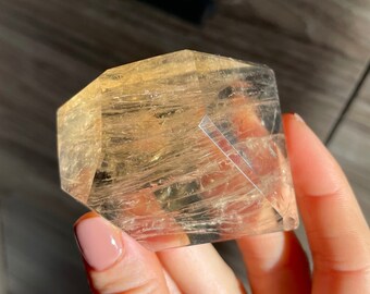 May include: A clear, faceted, golden citrine crystal with a diamond shape. The crystal has a natural, raw look with visible striations and inclusions.