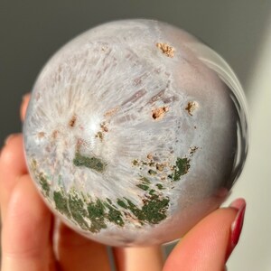 May include: A white and green agate sphere with a polished surface. The sphere has a swirling pattern of white, green, and brown.