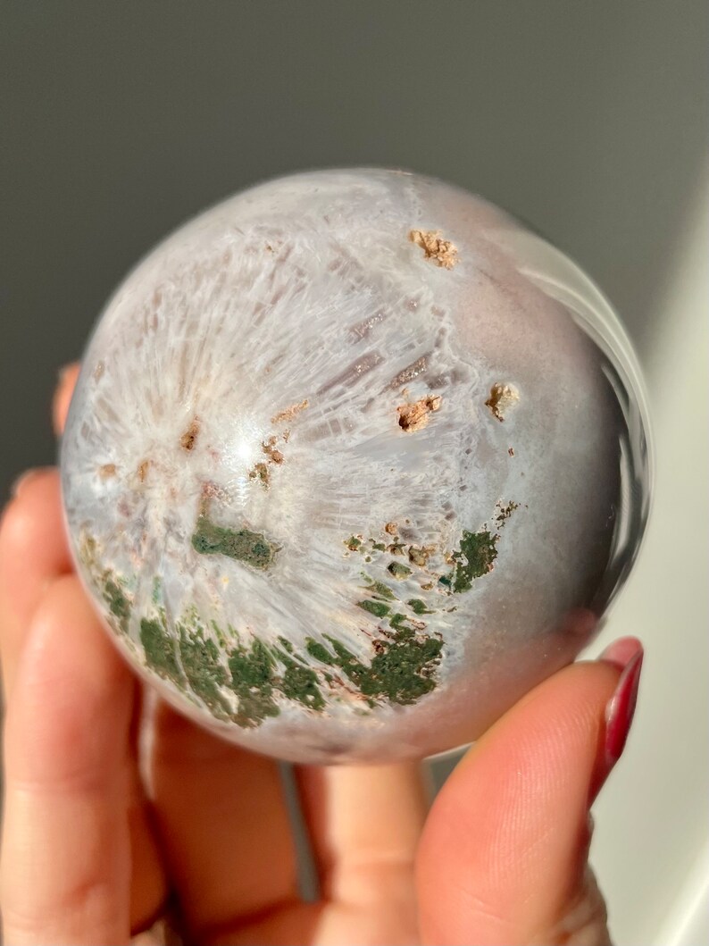 May include: A white and green agate sphere with a polished surface. The sphere has a swirling pattern of white, green, and brown.
