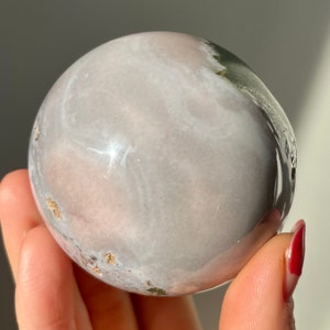 May include: A smooth, white and pink sphere with green and gold accents. The sphere is made of polished stone and has a swirling pattern.