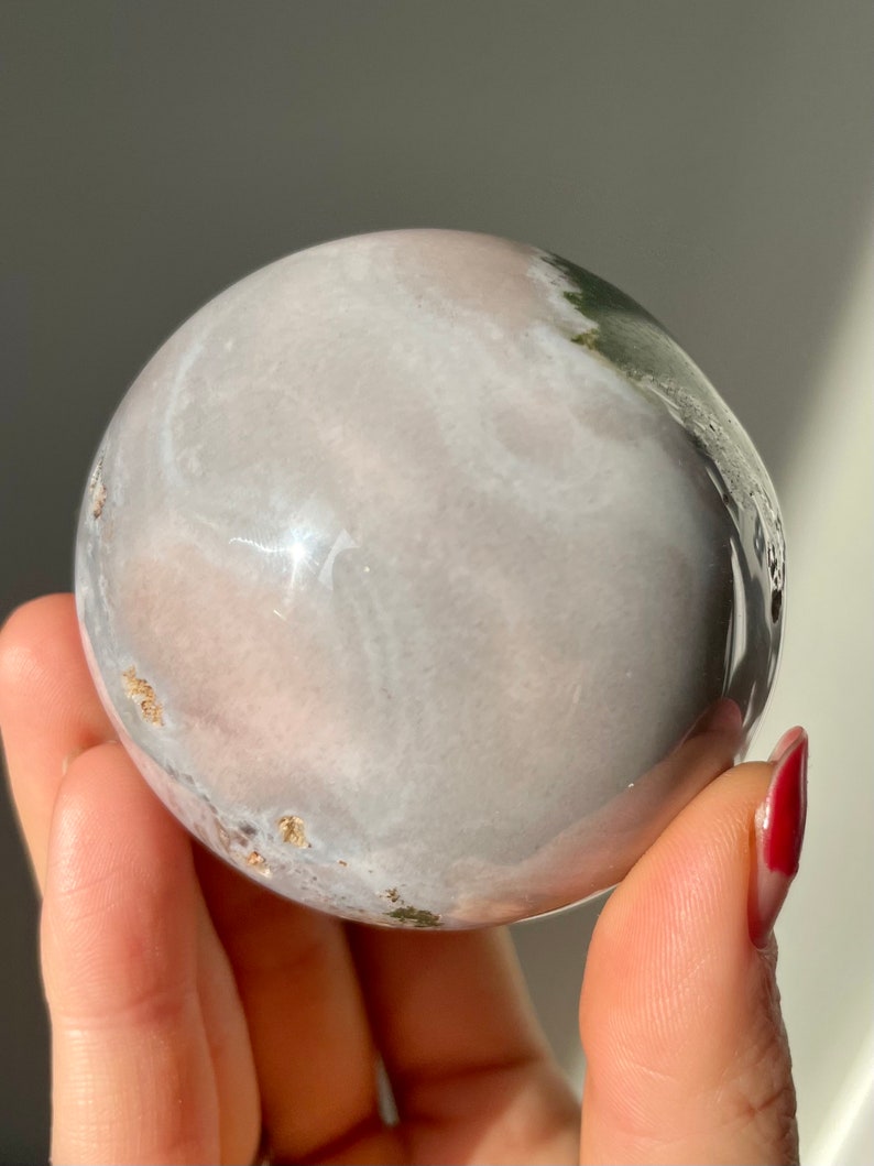 May include: A smooth, white and pink sphere with green and gold accents. The sphere is made of polished stone and has a swirling pattern.