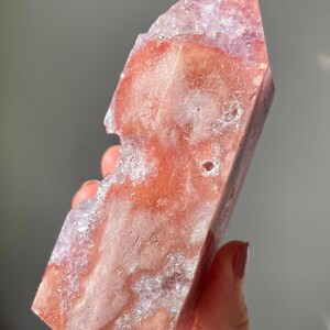 May include: A large, pink and purple amethyst crystal point with a rough, natural texture. The crystal has a unique, irregular shape and is partially translucent.