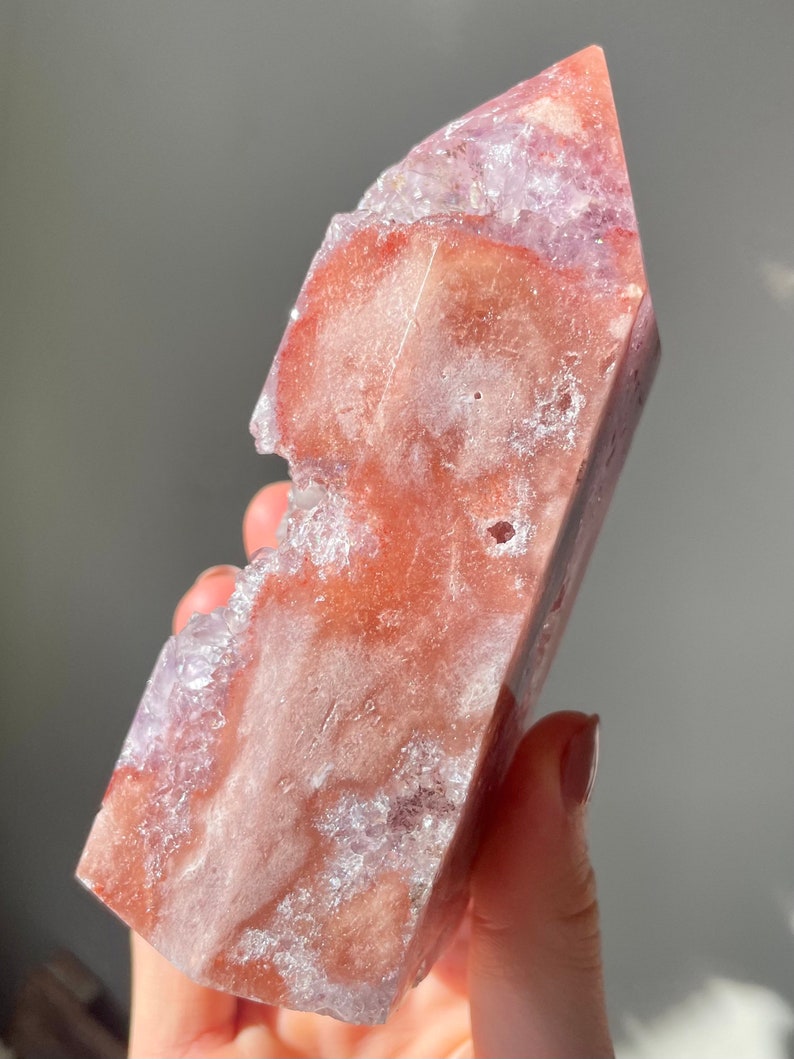 May include: A large, pink and purple amethyst crystal point with a rough, natural texture. The crystal has a unique, irregular shape and is partially translucent.