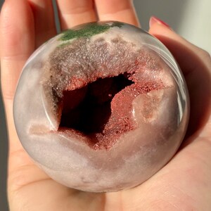 May include: A pink and white agate geode sphere with a large opening revealing a red and white crystal interior. The sphere is smooth and polished.