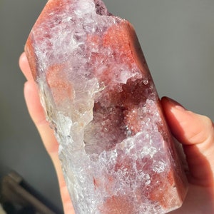 May include: A large, clear crystal point with a natural, druzy-like surface. The crystal is a deep red color with hints of purple and white. It has a large, open cavity on one side.