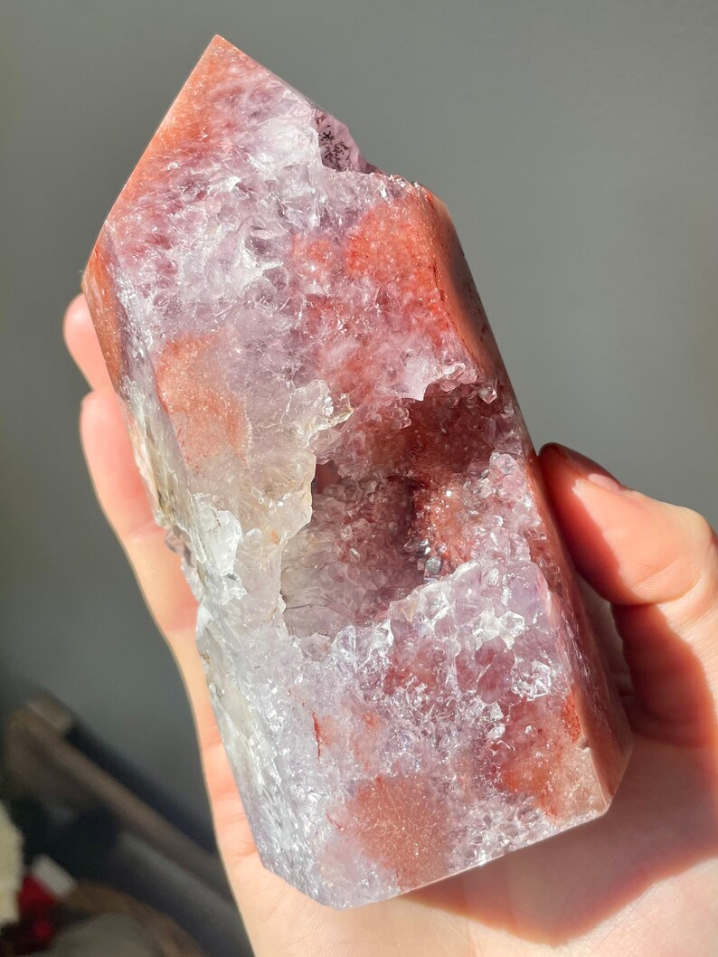 May include: A large, clear crystal point with a natural, druzy-like surface. The crystal is a deep red color with hints of purple and white. It has a large, open cavity on one side.