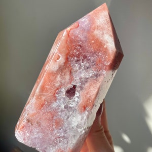 May include: A large, pink and white crystal point with a clear, druzy interior. The crystal has a natural, rough texture and is a beautiful example of a natural gemstone.