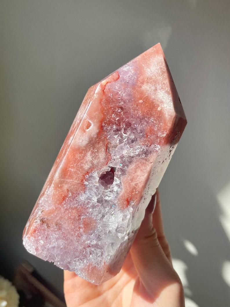 May include: A large, pink and white crystal point with a clear, druzy interior. The crystal has a natural, rough texture and is a beautiful example of a natural gemstone.